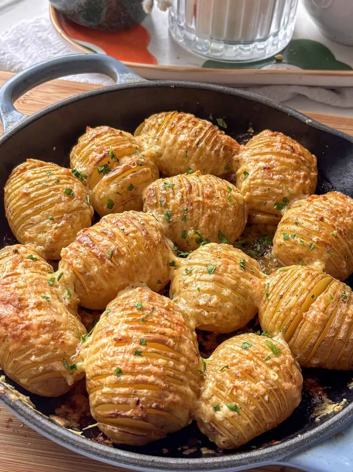 cheesy garlic hasselback potatoes in a skillet topped wuth parsley