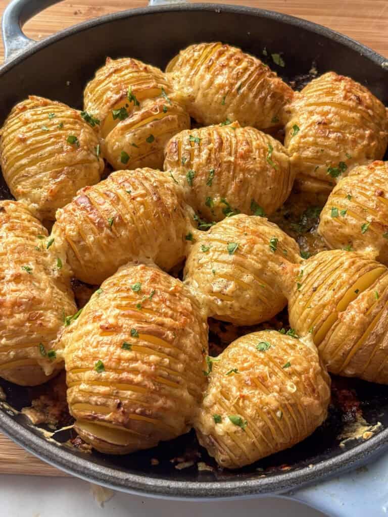 cheesy garlic hasselback potatoes in a skillet topped wuth parsley