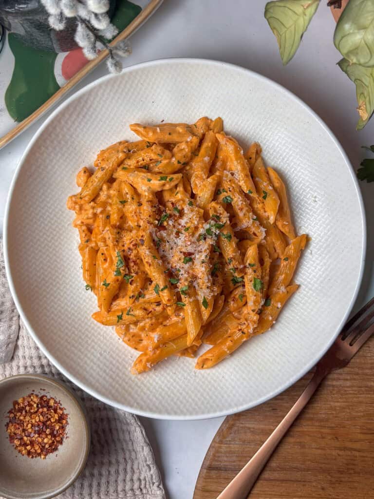 vodka pasta in a white dish topped with cheese, red pepper flakes, and parsley