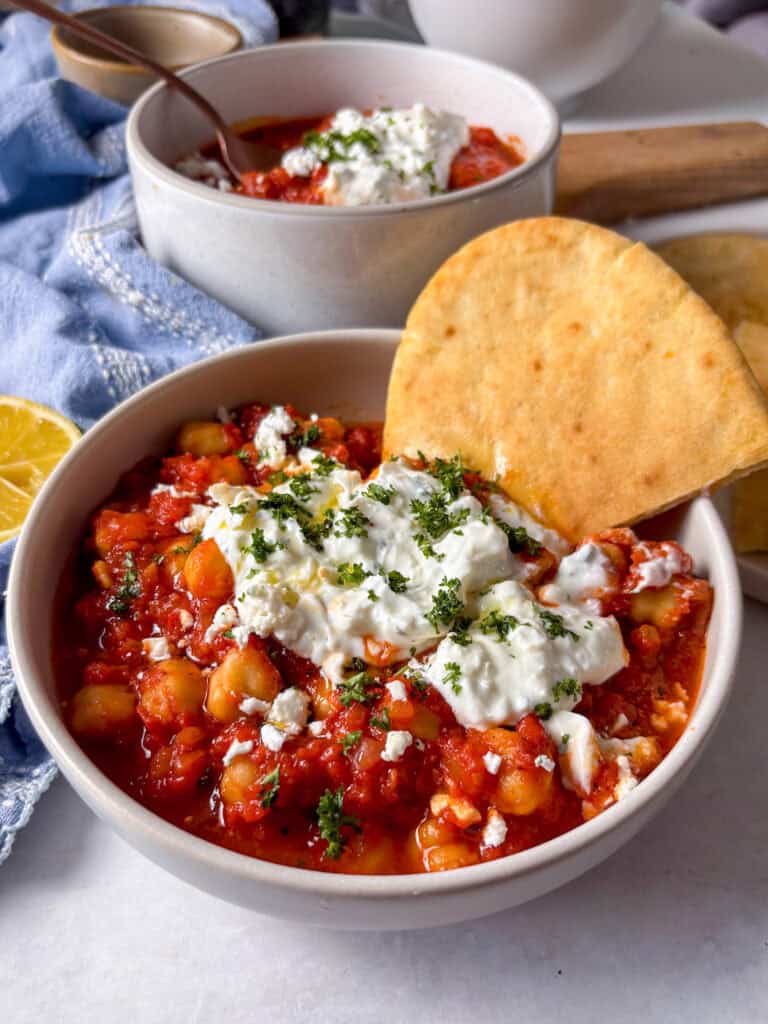 a bowl of harissa chickpeas topped with feta yoghurt sauce and fresh parsley, with toast pitta on the side