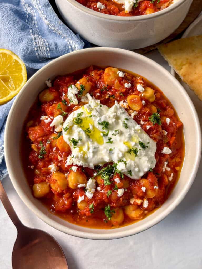 a bowl of smoky harissa chickpeas topped with feta yofhurt sauce, more feta, and parsley