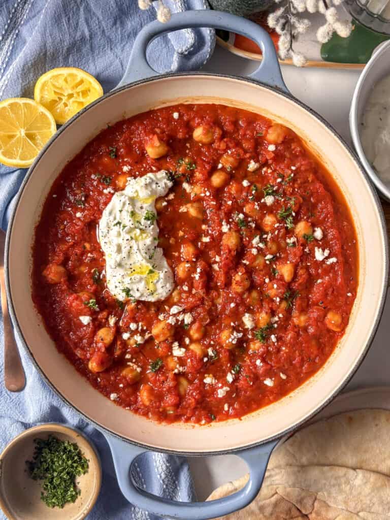 a casserole pan of smoky harissa chickpeas topped with feta yoghurt sauce and crumbled feta and frsh parsley