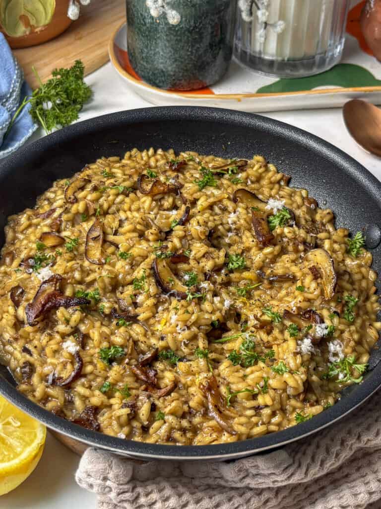 mushroom risotto in a pan, topped with roasted mushrooms and fresh parsley