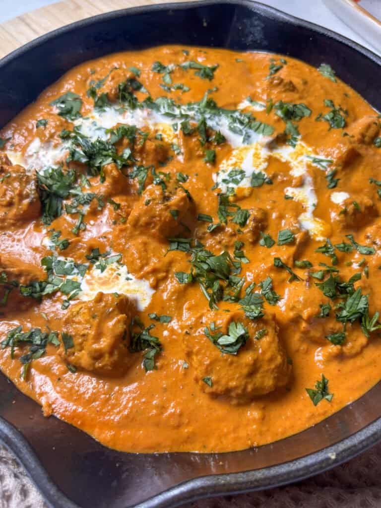 silky tofu tikka masala in a pan, topped with chopped cilantro and a drizzle of cream