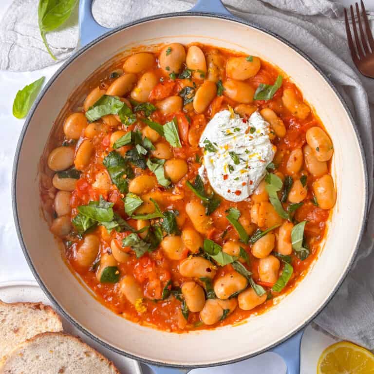 a casserole pan of cherry tomato ricotta butter beans, with a scoop of ricotta, fresh basil, and topped with lemon zest and red chili flakes