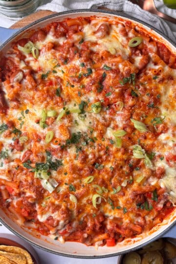 a casserole pan of chili mac and cheese with a golden cheesy topping scattering with sliced scallions and fresh chopped cilantro