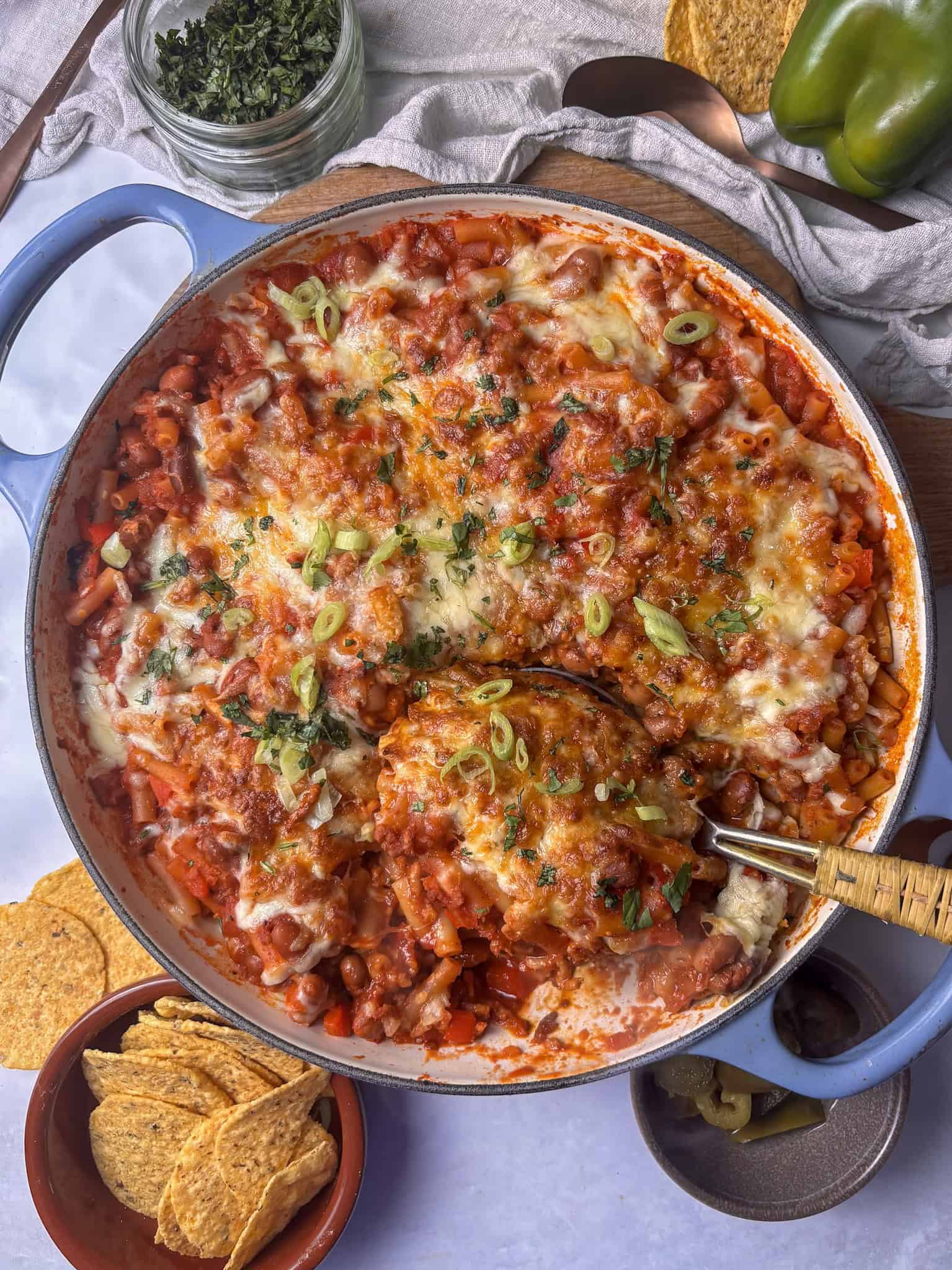 a casserole pan of chili mac and cheese with a golden cheesy topping, and a scattering of scallions and fresh chopped cilantro