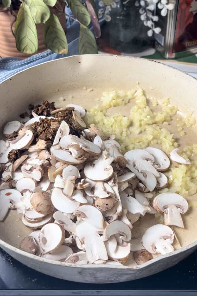 sliced chestnut mushrooms and porcini mushrooms added to the pan with diced onions and garlic