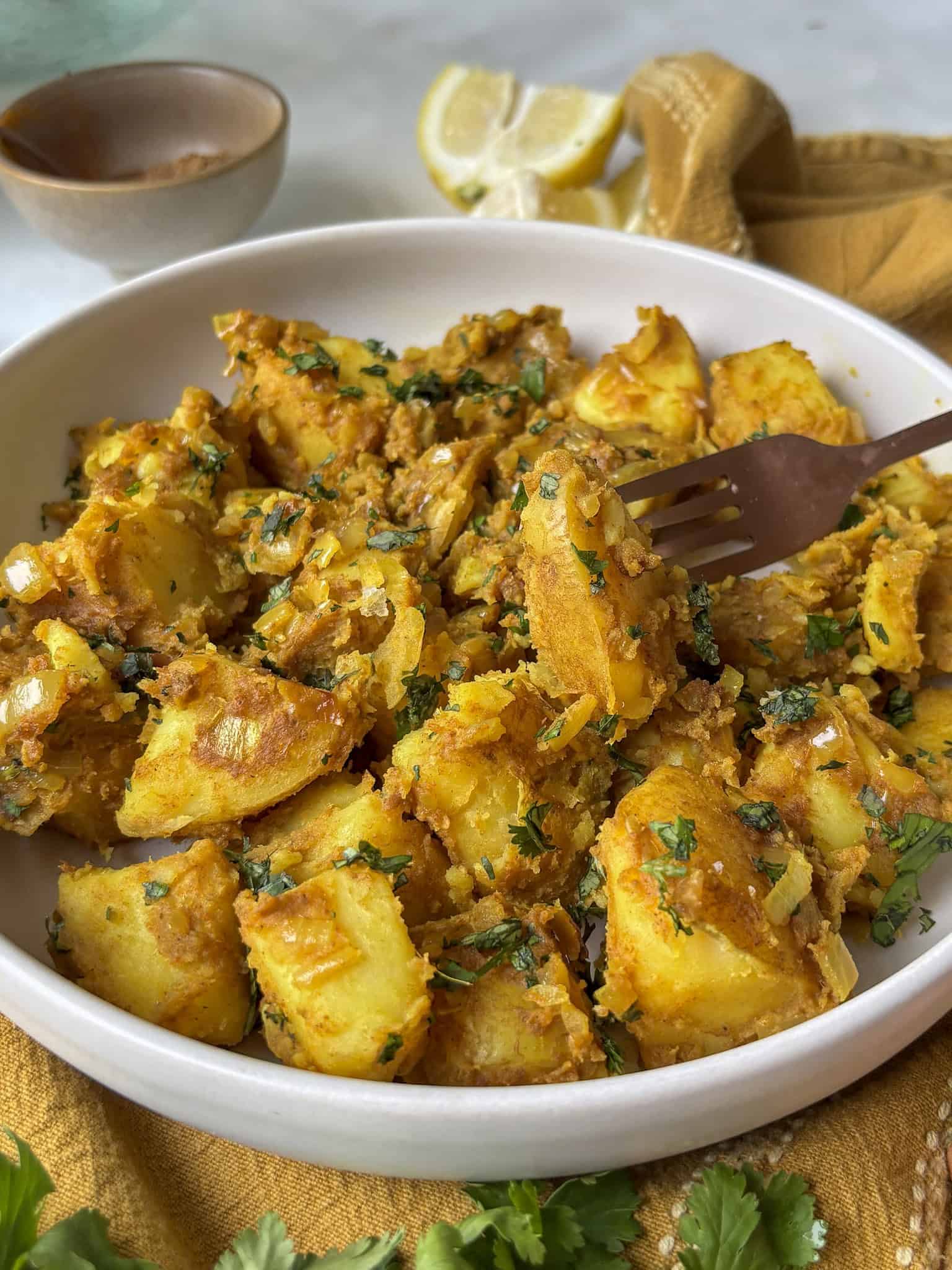 a close up shot of curried potatoes in a bowl topped with fresh cilantro - with a fork taking a potato out of the bowl