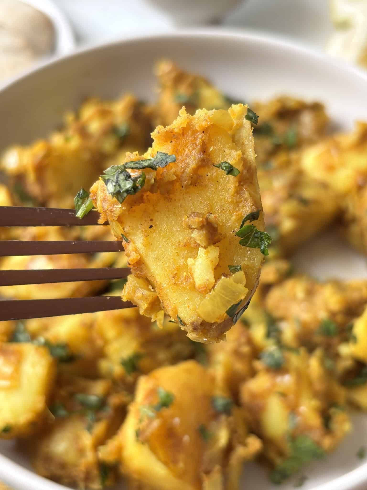 a curried potato speared by a fork is in focus in the foreground, with the remaining bowl seen in the background out of foucs