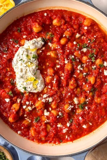a pan of harissa chickpeas topped with feta yogurt sauce and fresh parsley