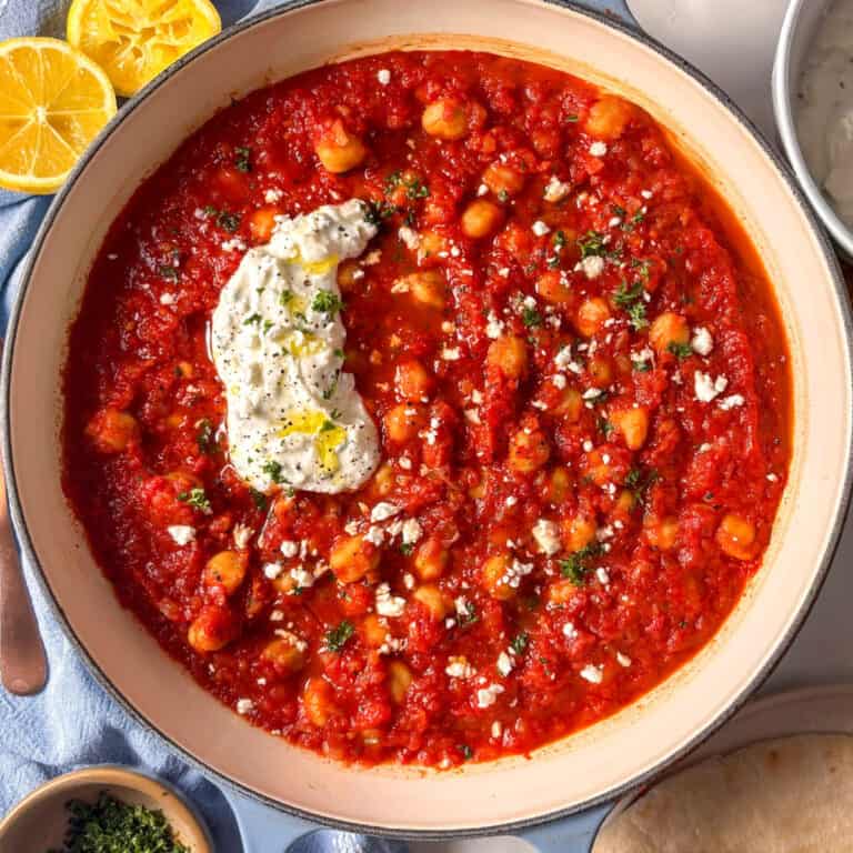 a pan of harissa chickpeas topped with feta yogurt sauce and fresh parsley