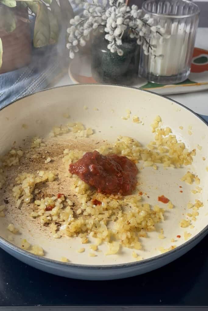 harissa paste and tomato paste are added to the pan along with the sauted diced onion and garlic