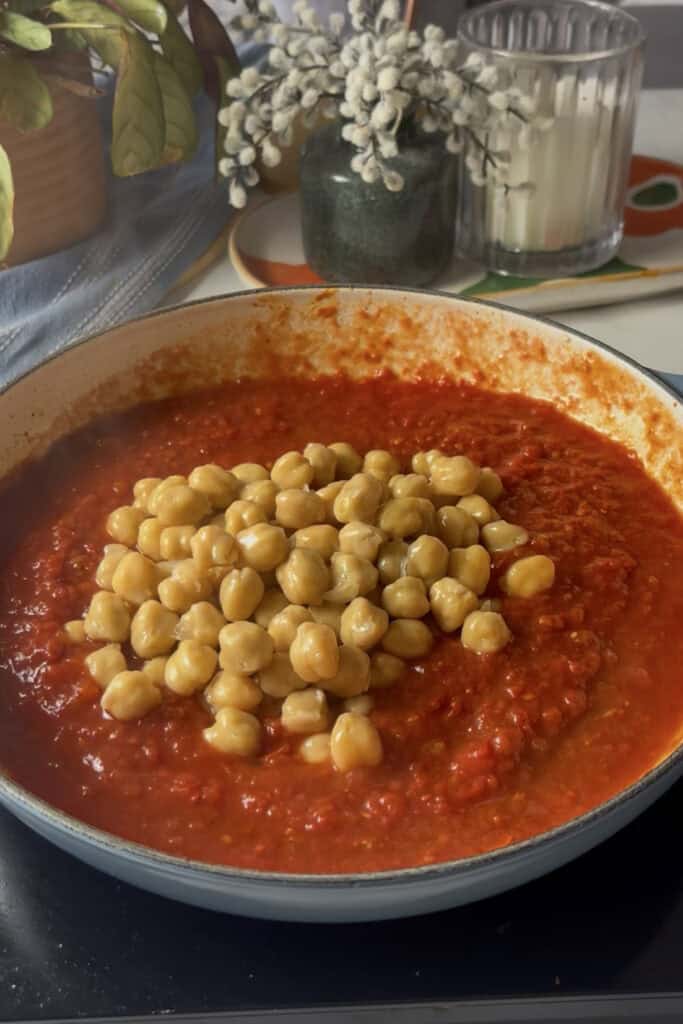 chickpeas, freshly added to the casserole pan, sit on top of a harissa tomato sauce in a casserole pan