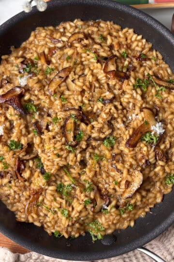 a pan of mushroom risotto topped with caramelised roasted mushroom, pecorino cheese, and fresh parsley