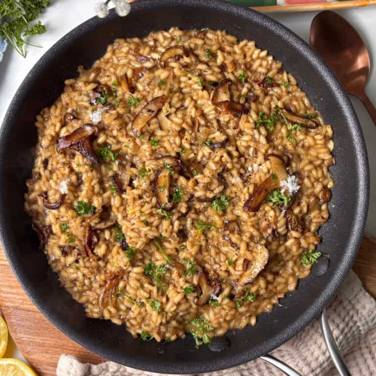 a pan of mushroom risotto topped with caramelised roasted mushroom, pecorino cheese, and fresh parsley