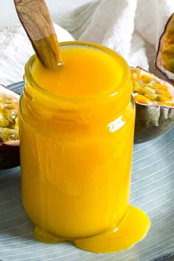 a jar of passion fruit curd with passion fruit halves in the background and a spoon in the jar