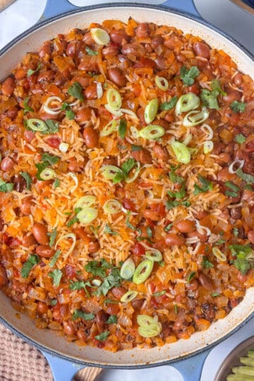 a casserole pan of spanish rice and beans topped with cilanto and sliced spring onions