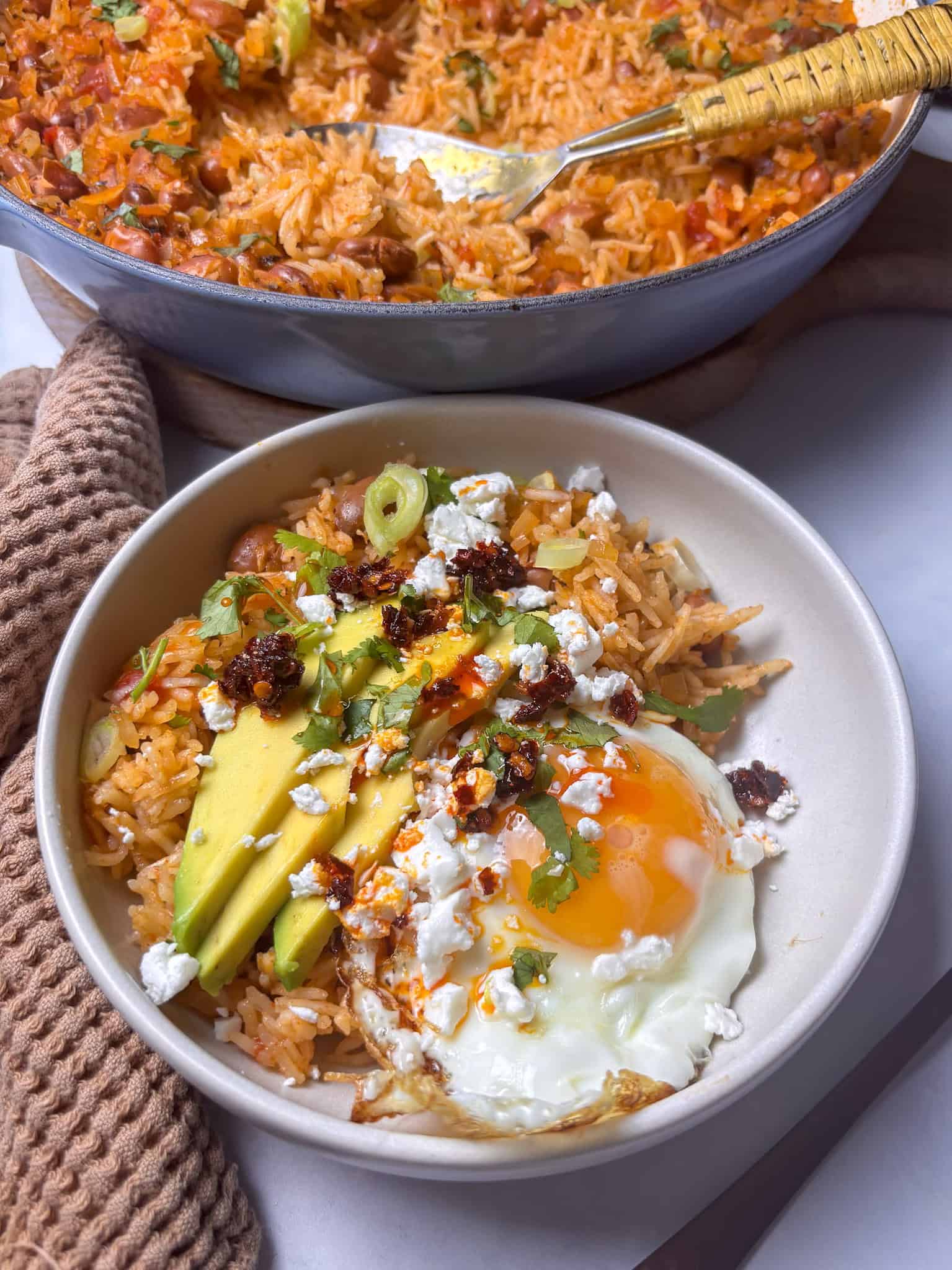 a bowl of Spanish rice and beans served with a fried egg, sliced avocado, crumbled feta, and chili crisp.