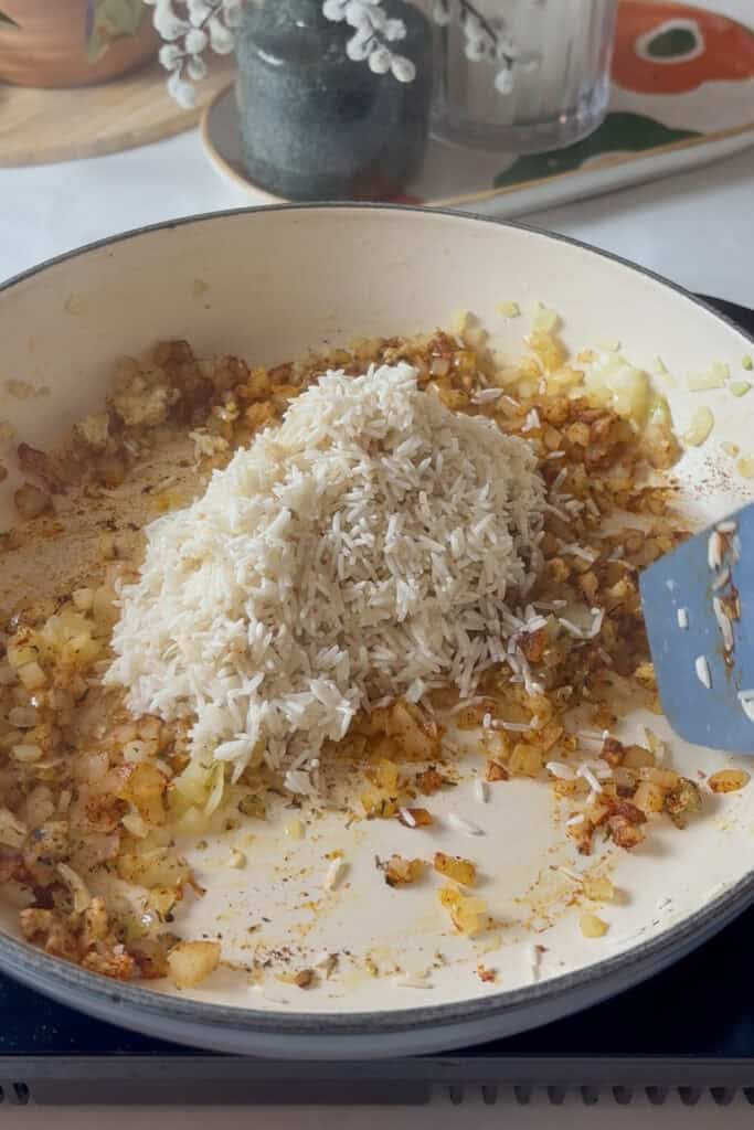 Washed white rice added to the pan of spices and onions