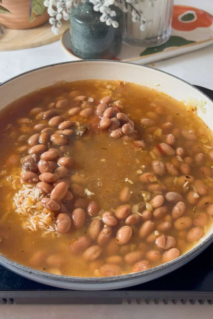 salsa, pinto beans, and vegetable broth added to the pan of rice and onions ready to simmer