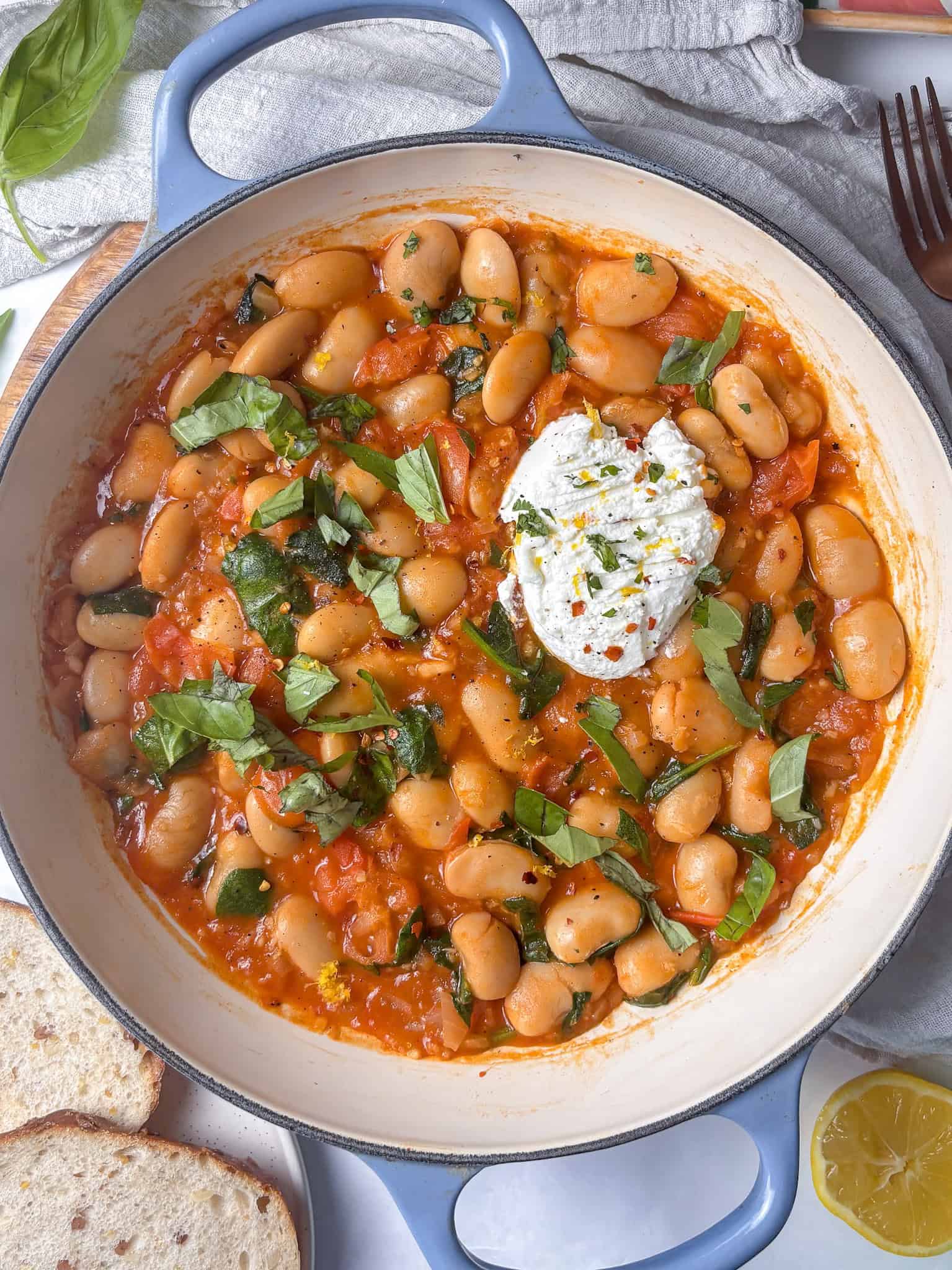 pan of cherry tomato butter beans topped with ricotta, chili flakes, basil, and lemon zest