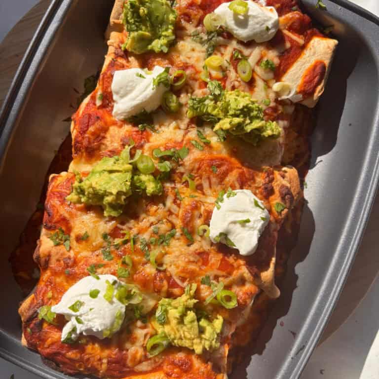 a tray of buffalo white bean enchiladas topped with sour cream, guacamole, spring onions, and cilantro