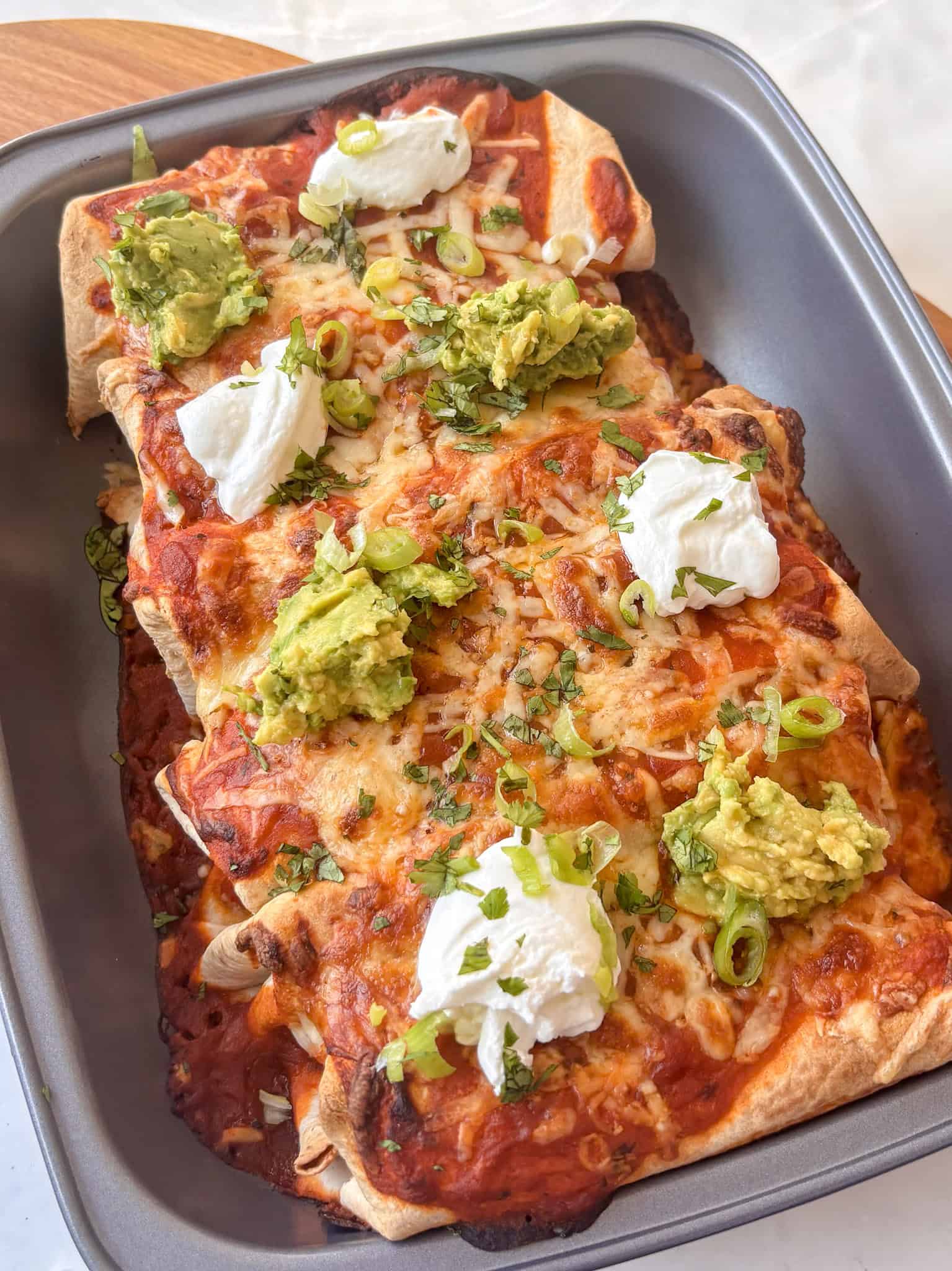 a pan of buffalo white bean enchiladas topped with sour cream, guacamole, and sliced spring onion
