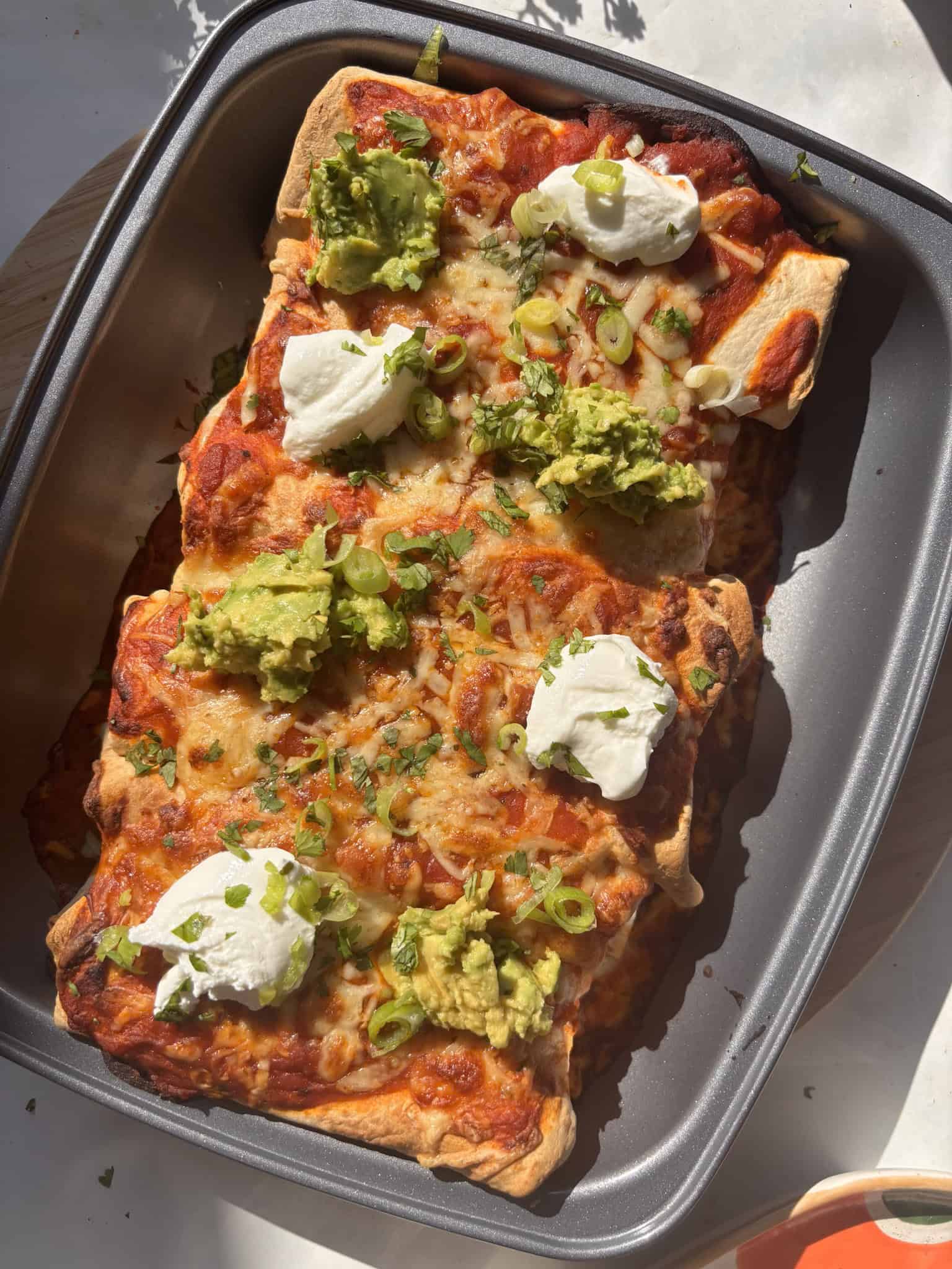 buffalo white bean enchiladas in the sunshine, topped with avocado and sour cream