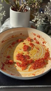 tomato paste being stirred into diced shallots and minced garlic