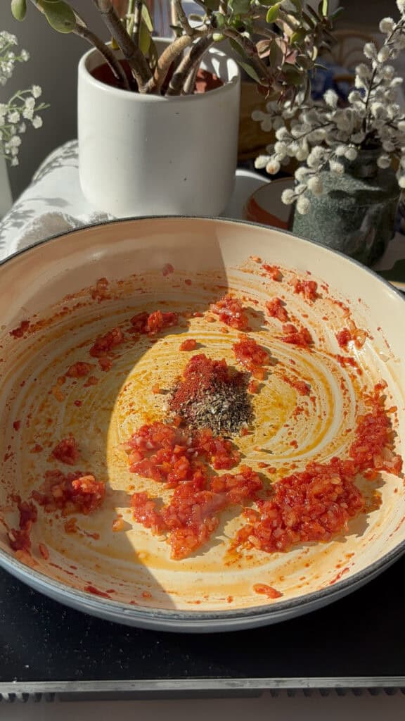 seasonings added to a pan with the tomato paste and diced shallots and minced