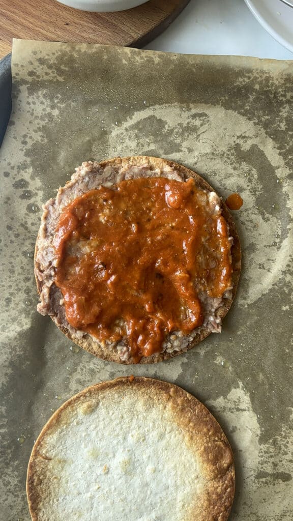 two crispy tortilla wraps, one topped with refried beans and enchilada sauce