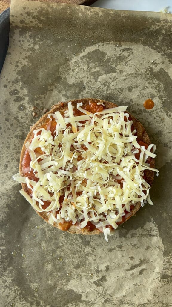 a crispy Mexican pizza pre-cooking topped with enchilada sauce and grated cheese