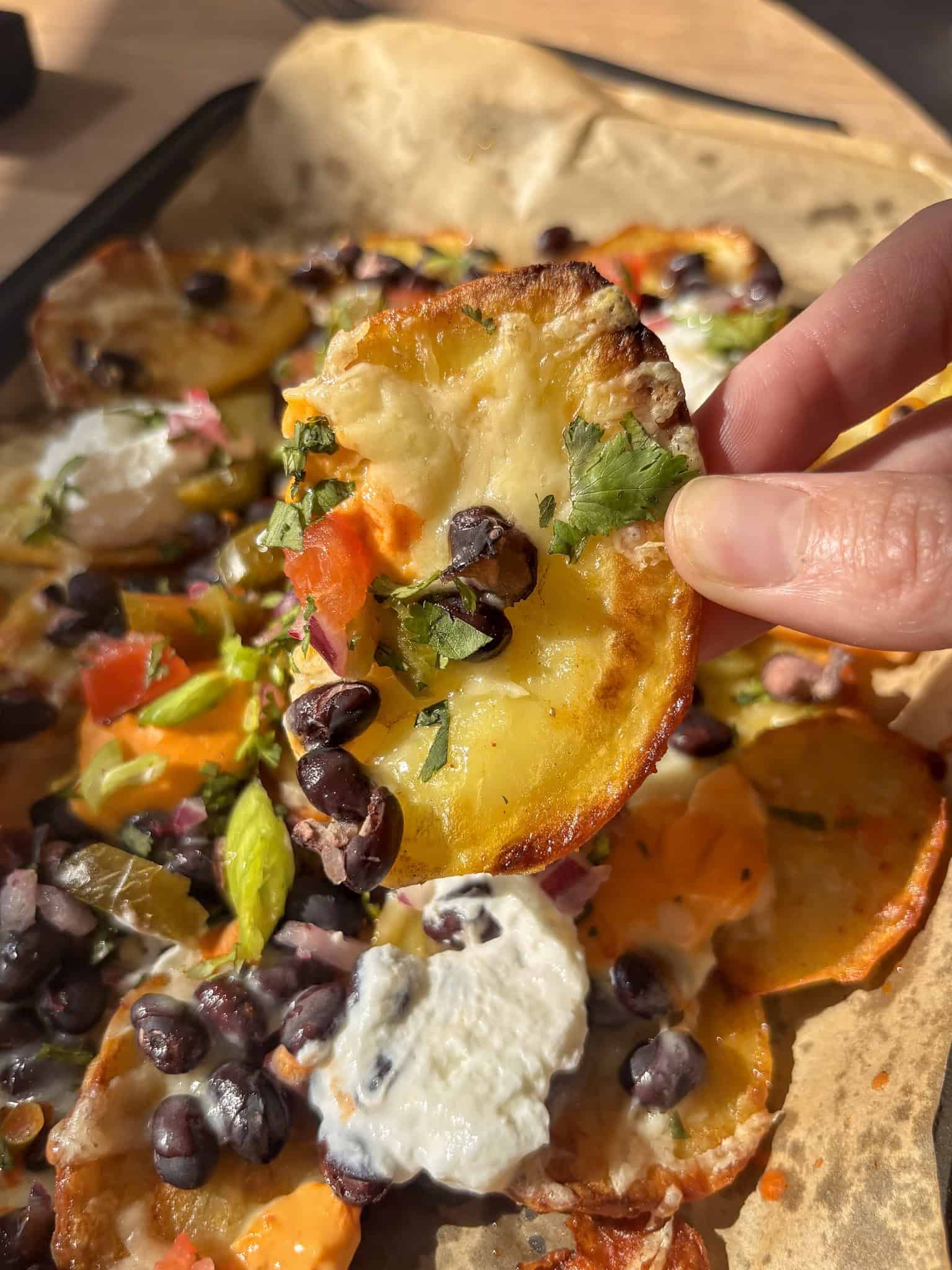 a slice of baked potato with melted cheese, black beans, toppings on it held over the remaining potato nachos