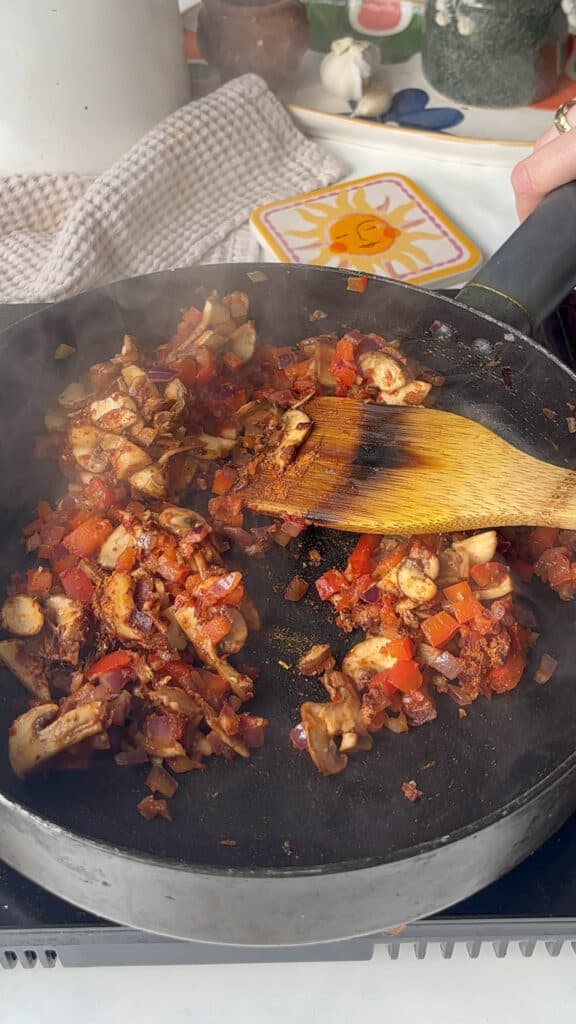 tomato paste and seasonings are stirred into sauted vegetables in a saucepan, building the base for the tomato sauce