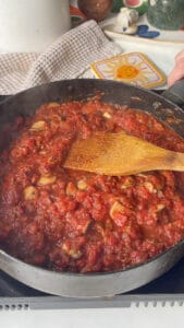 a tomato sauce being simmered in a saucepan with red pepper, mushrooms, onions, and garlic