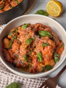 a white bowl loaded with creamy sausage gnocchi topped with Pecorino cheese, black pepper, and chili oil