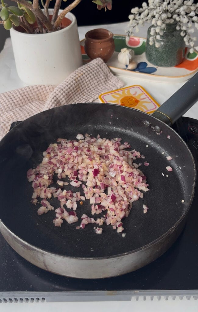 diced red onion and minced garlic being cooked in a pan in oil