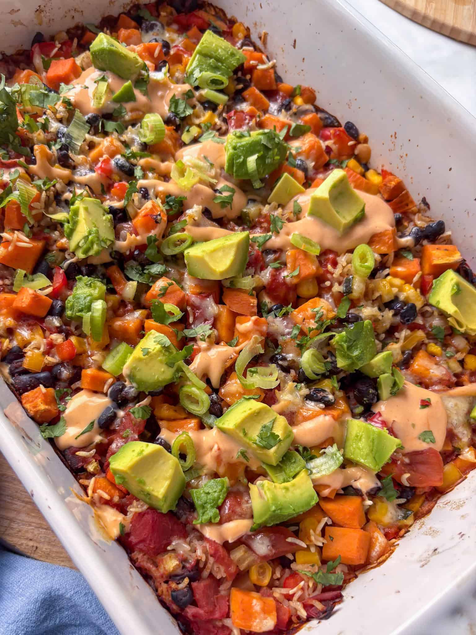 a casserole dish of black bean casserole, topped with cubed avocado, cilantro, and a buffalo sauce