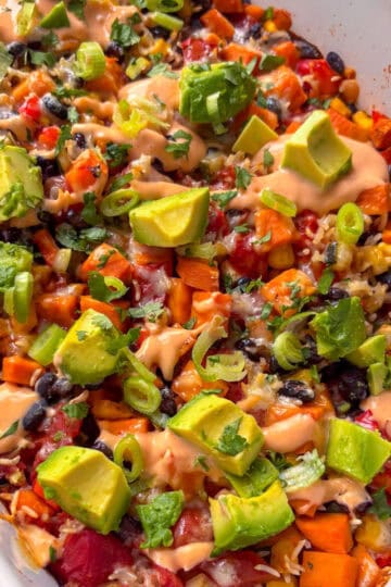 a casserole dish of black bean casserole topped with cubed avocado, cilantro, and spring onion
