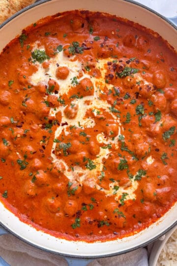 a casserole pan of creamy chickpea tikka masala topped with cream, cilantro, and red chili flakes