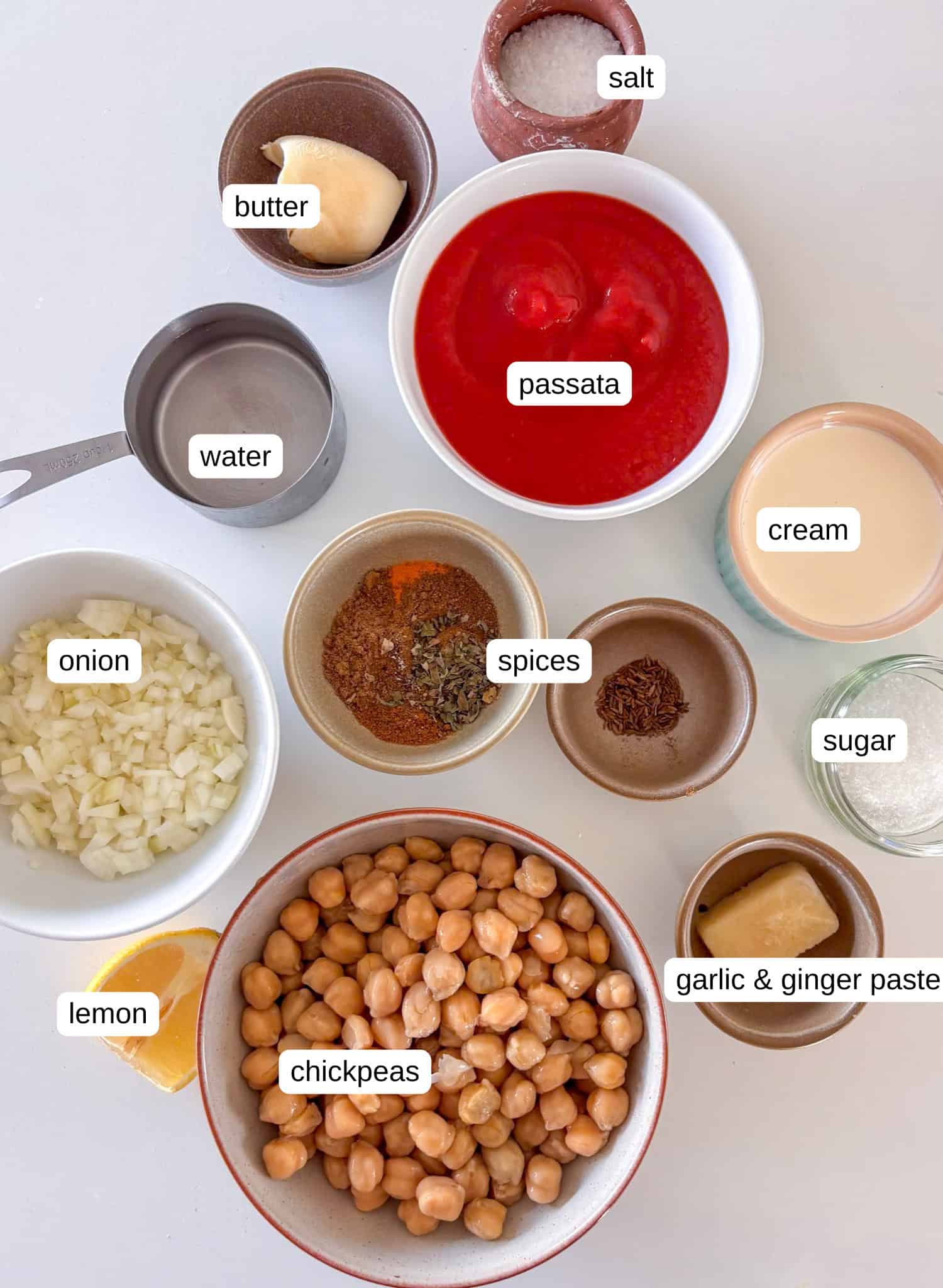 ingredients in bowls ready to make a chickpea tikka masala - including drained cooked chickpeas, passata, onion, garlic and ginger paste, butter, sugar, cream, lemon