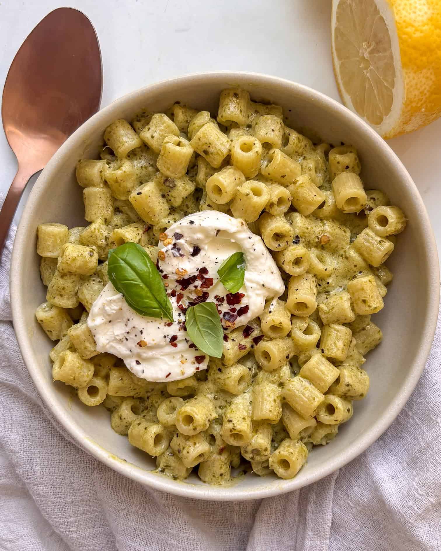 a bowl of creamy pesto ditalini pasta topped with creamy burrata, chili flakes, and basil