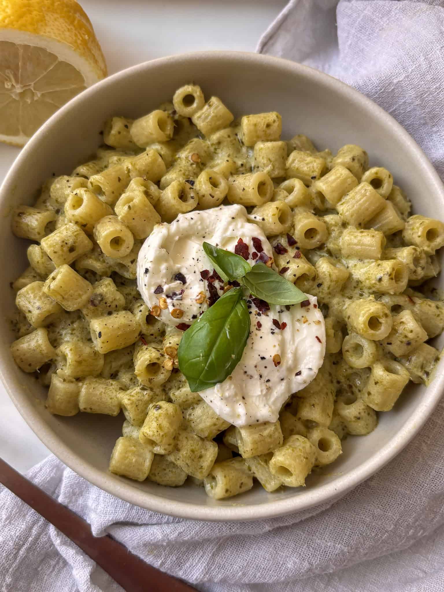 a bowl of creamy pesto ditalini pasta topped with creamy burrata, chili flakes, and basil