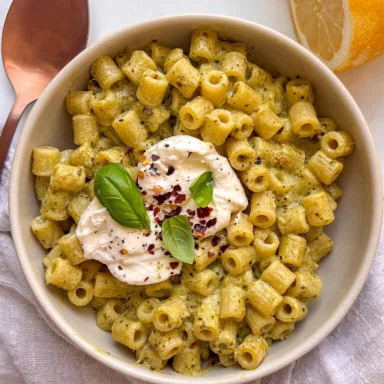 a bowl of creamy pesto ditalini pasta topped with creamy burrata, chili flakes, and basil