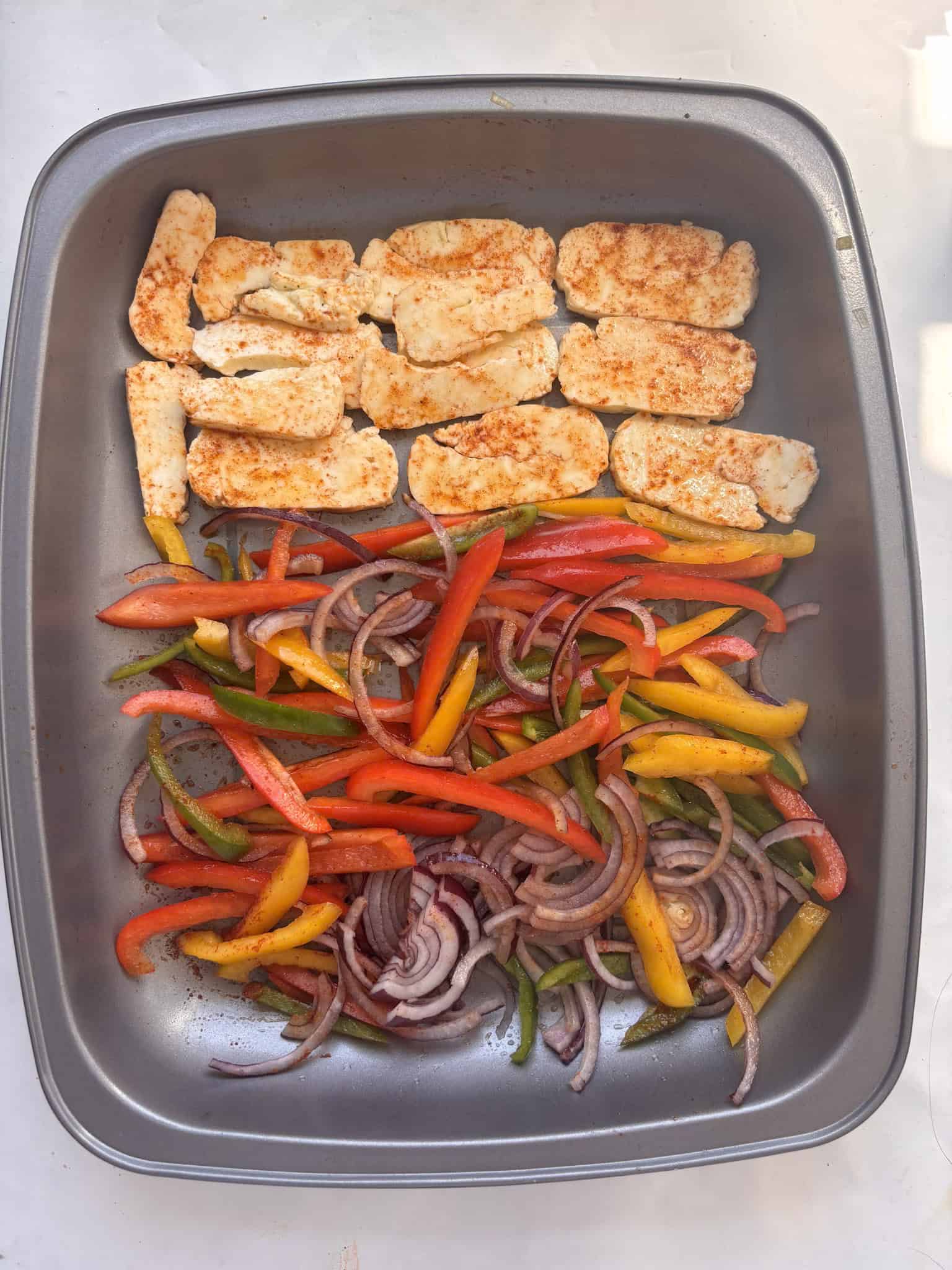 seasoned halloumi, peppers and red onions in a baking tray ready to be roasted