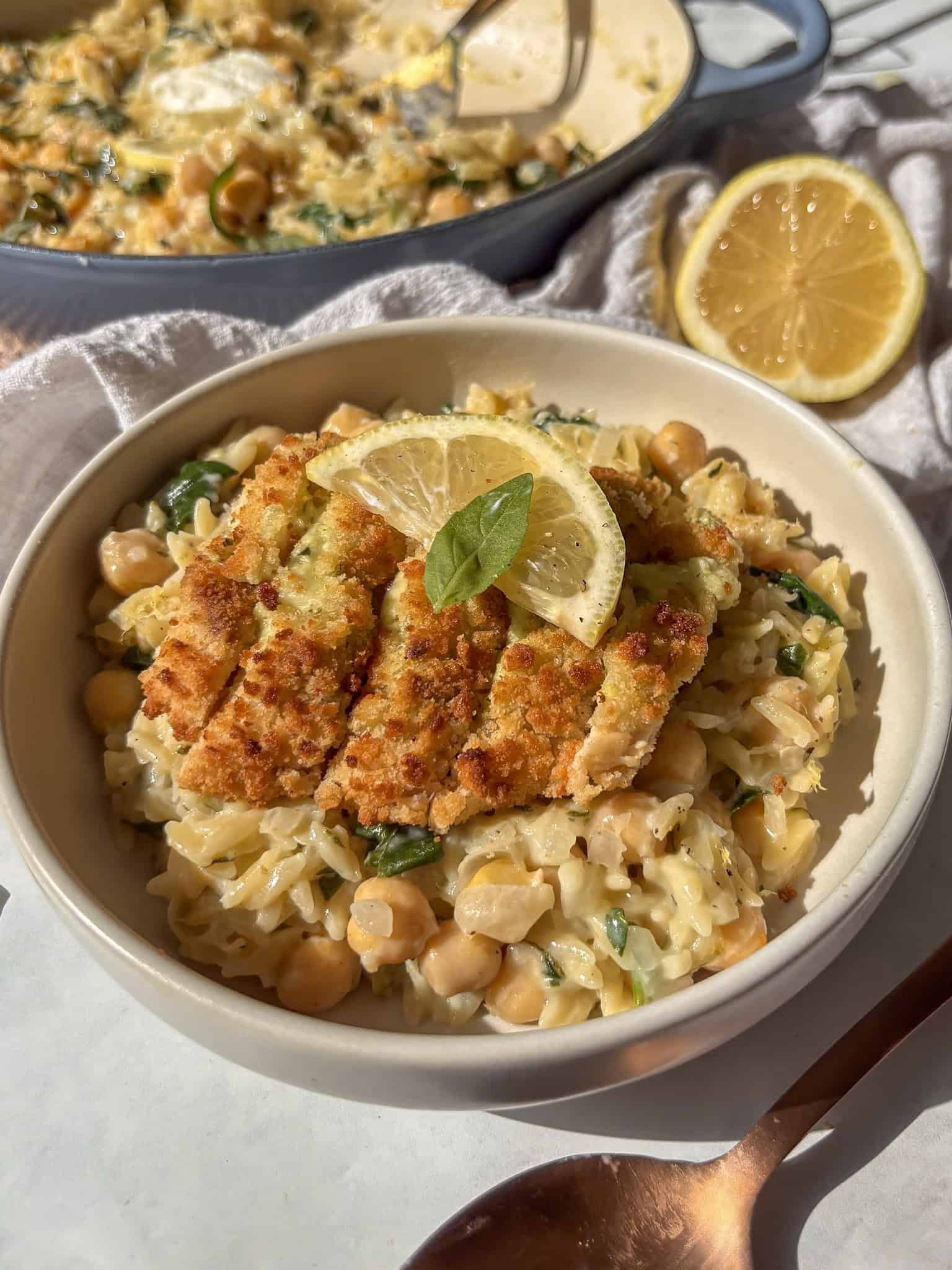 creamy lemon orzo in a bowl topped with a breaded vegetarian chicken fillet and a slice of lemon