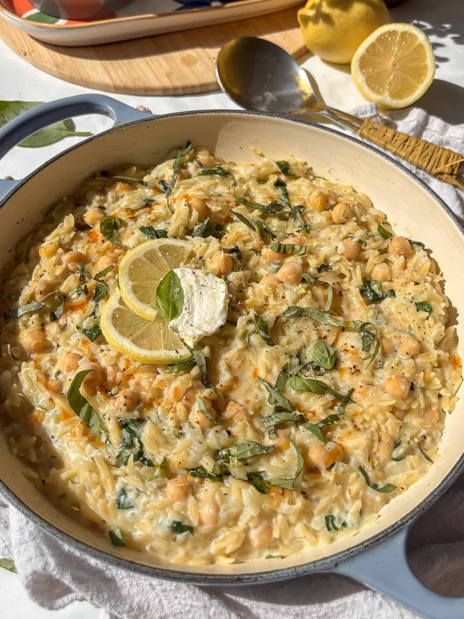 creamy lemon orzo in a casserole pan topped with fresh basil and lemon slices