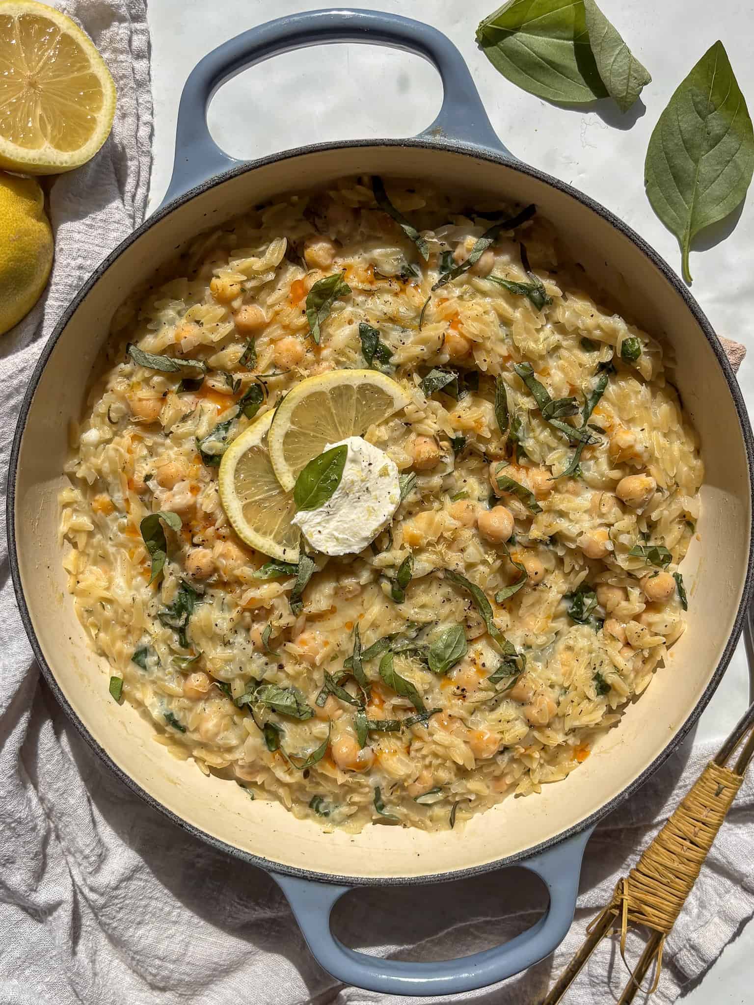 creamy lemon orzo in a pan topped with fresh basil, slices of lemon and cream cheese