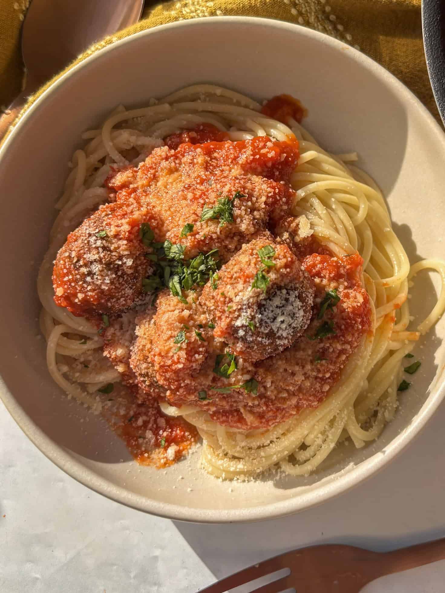 lentil meatballs in a tomato sauce on top of spaghetti with a dusting of parmesan and fresh herbs
